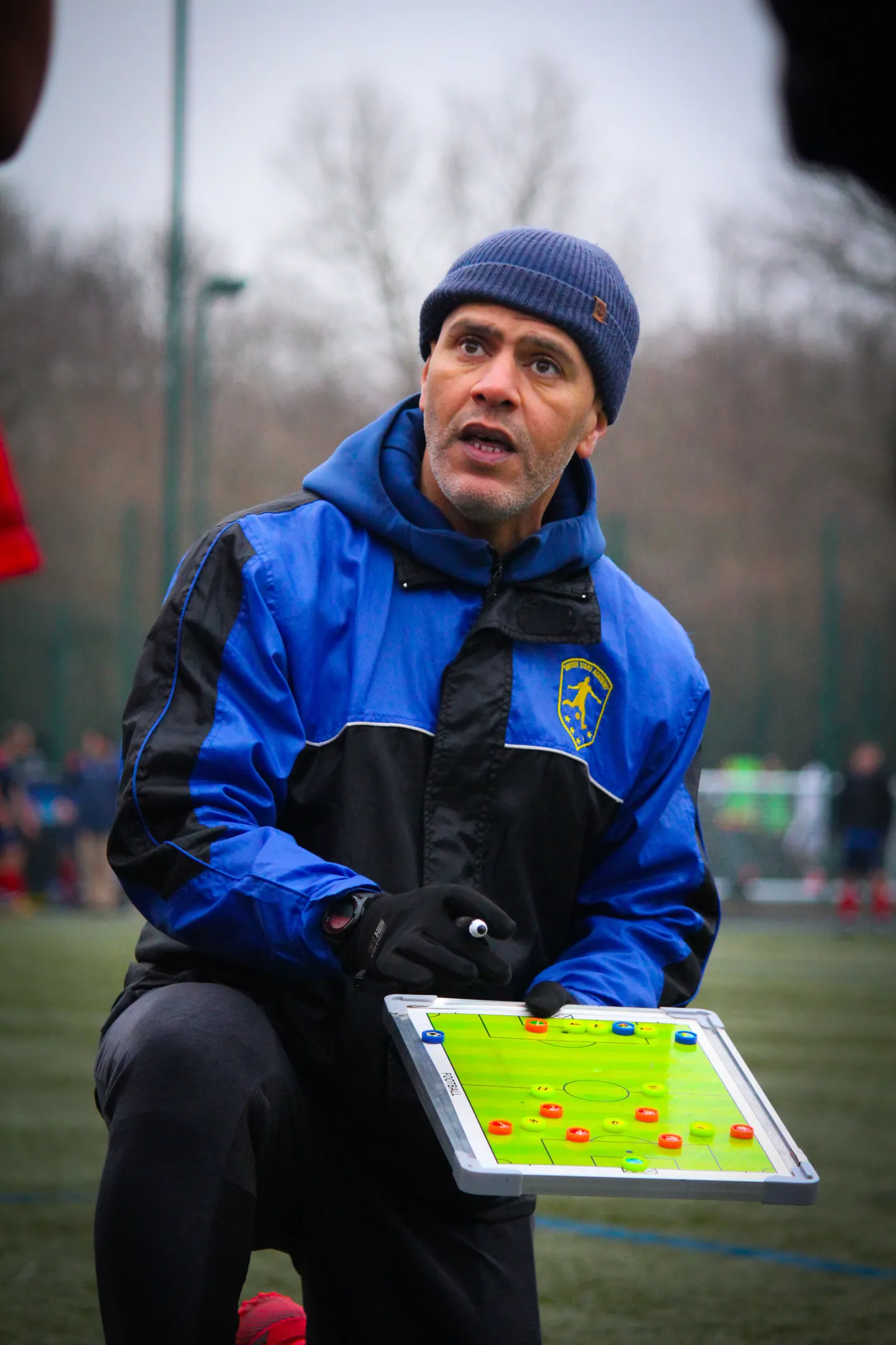A football coach explaining a training strategy beside the pitch.