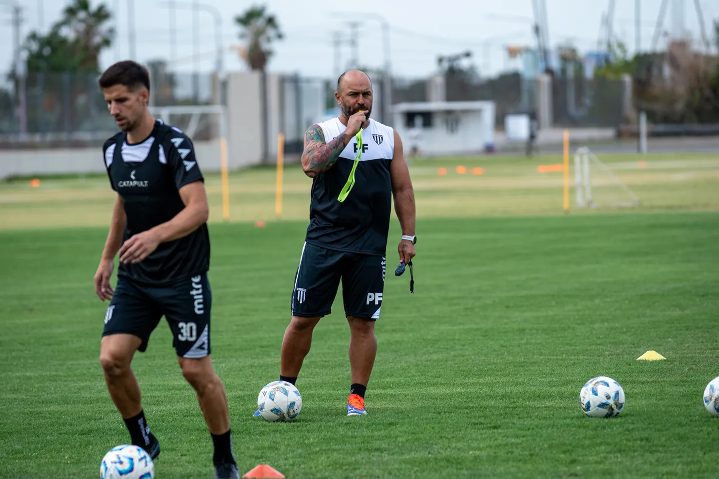 A coach organising football players during training on a green pitch.
